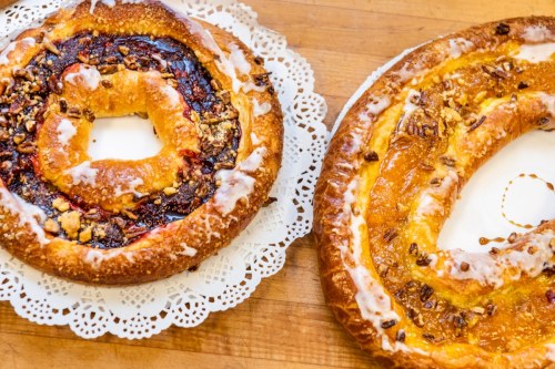 Two circular pastries on lace doilies, one with a berry filling and nuts, the other with an orange filling and icing.