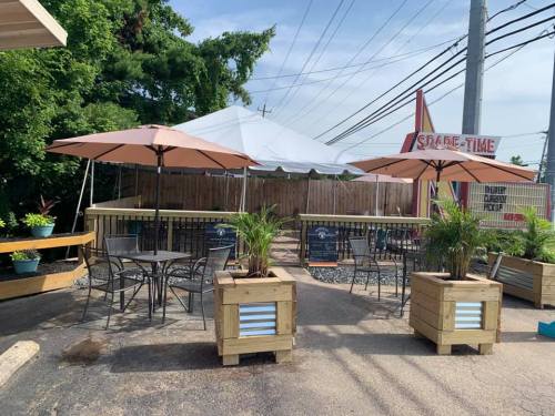 Outdoor seating area with tables, umbrellas, and planters, featuring a tent in the background and a sign for "Spade-Time."