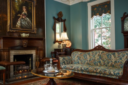 A cozy living room featuring a vintage sofa, ornate decor, a fireplace, and a large portrait on the wall.
