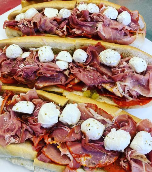 Three hoagie rolls filled with layers of deli meats and topped with small mozzarella balls.