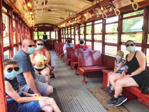 A family wearing masks and sunglasses sits inside a vintage trolley, with empty seats around them.