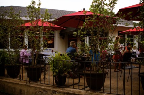Outdoor dining area with red umbrellas, potted plants, and patrons enjoying their meals at a restaurant.