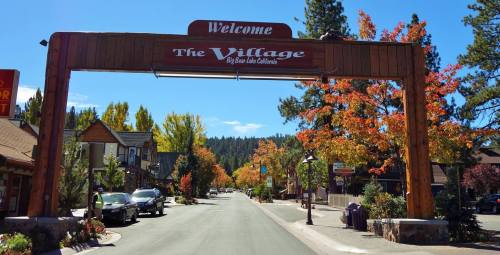 A wooden archway welcomes visitors to The Village in Big Bear Lake, California, lined with colorful autumn trees.