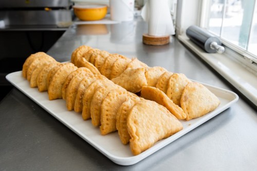 A tray of golden-brown, freshly baked pastries arranged neatly on a stainless steel countertop.