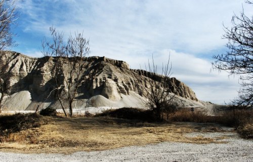 A barren landscape featuring a large, rocky hill and sparse trees under a cloudy sky.