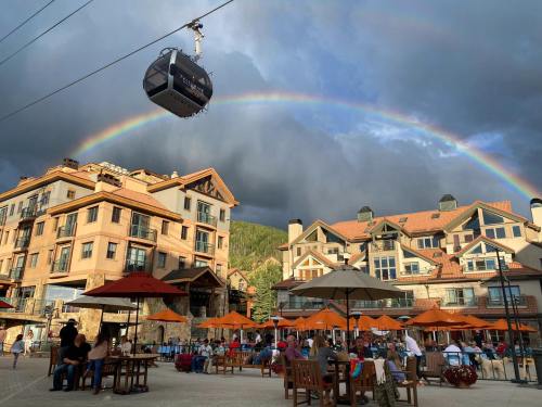 A scenic view of a resort with a rainbow overhead, featuring outdoor seating and a gondola in the foreground.
