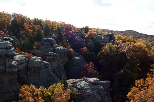 Rocky cliffs surrounded by vibrant autumn foliage under a bright sky.