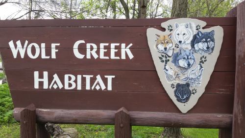 Sign for Wolf Creek Habitat featuring a shield with painted wolves and the text "Wolf Creek Habitat."