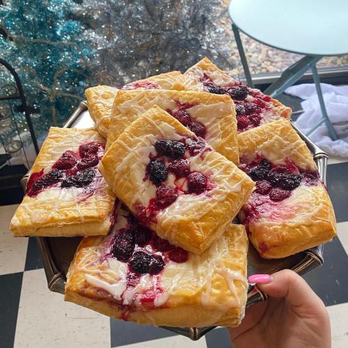 A hand holding a tray of golden pastries topped with mixed berries and drizzled with white icing.