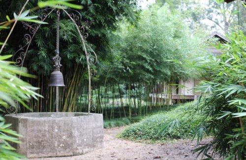 A serene garden scene featuring a stone well with a bell, surrounded by lush bamboo and greenery.