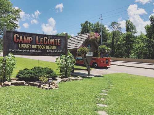 Sign for Camp LeConte Luxury Outdoor Resort with a colorful shuttle bus parked nearby, surrounded by greenery and blue skies.