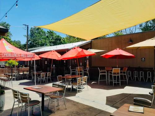 Outdoor dining area with red umbrellas, wooden tables, and a sunny sky.
