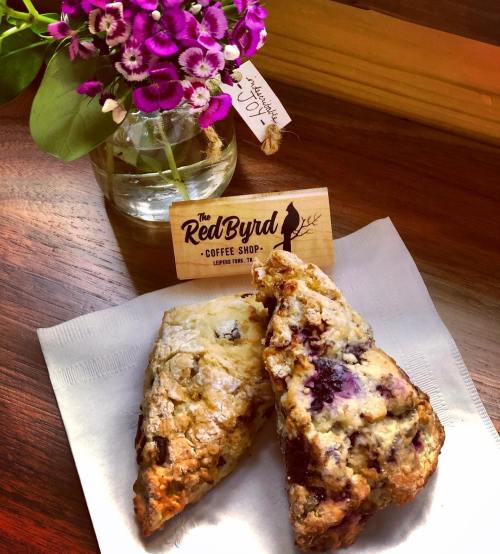 A close-up of two scones on a napkin, with a small vase of purple flowers and a sign for The Red Byrd Coffee Shop.