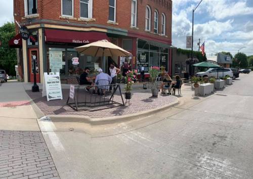 Outdoor seating area at Skillet Cafe with patrons enjoying their meals, surrounded by flowers and a sunny sky.