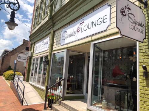 Exterior view of Sipside Lounge, featuring large windows and signage, with a sunny street scene in the background.