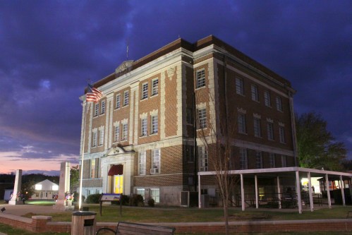 Historic brick building at dusk, featuring an American flag and surrounded by trees and benches.