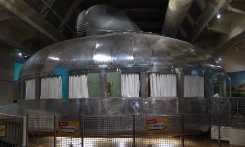 A large, shiny metallic structure resembling a futuristic dome with windows and curtains, displayed indoors.
