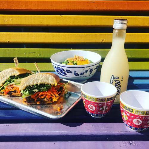 A colorful meal featuring two sandwiches, a bowl of salad, a bottle of drink, and two decorative cups on a vibrant background.