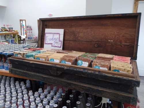 A wooden chest filled with various fudge flavors, displayed in a shop with colorful products in the background.