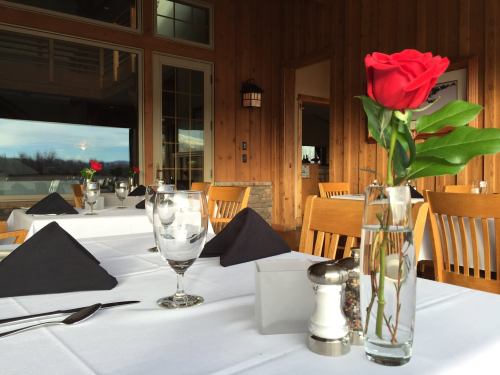 A cozy restaurant setting with wooden walls, a table set with a rose, glasses, and black napkins.