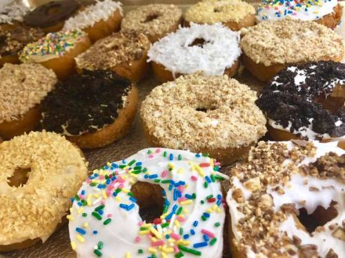 A variety of colorful donuts with different toppings, including sprinkles, coconut, and crushed cookies, arranged on a tray.