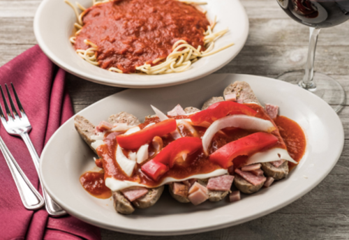 A plate of sausage topped with red peppers, onions, and sauce, alongside a bowl of spaghetti with marinara sauce.