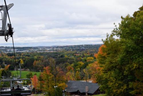 A scenic view from a chairlift, showcasing vibrant autumn foliage and a cloudy sky over a landscape.