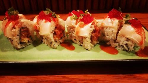 A plate of sushi rolls topped with sliced fish, roe, and green onions, served on a green dish.