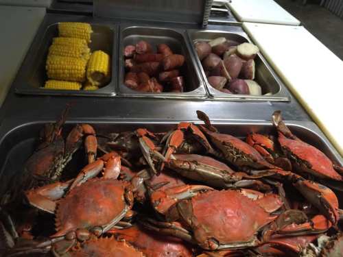 A tray of cooked crabs in front, with corn, sausage, and potatoes in containers behind.