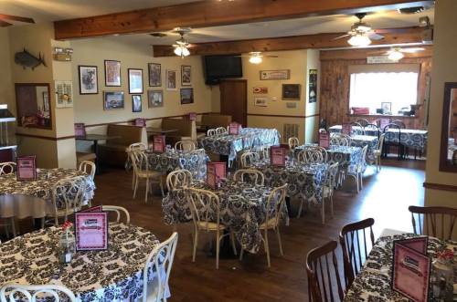 A cozy restaurant interior with tables covered in black and white lace tablecloths, decorated walls, and wooden accents.