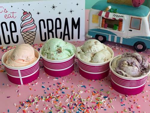 Four colorful ice cream scoops in pink cups, surrounded by colorful sprinkles, with an ice cream truck backdrop.