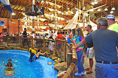 A lively seafood restaurant with a pirate theme, featuring a pool and guests watching a performer in a wetsuit.