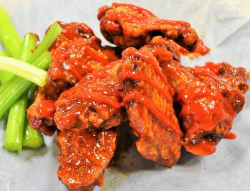 A plate of spicy chicken wings coated in red sauce, served with fresh celery sticks on the side.
