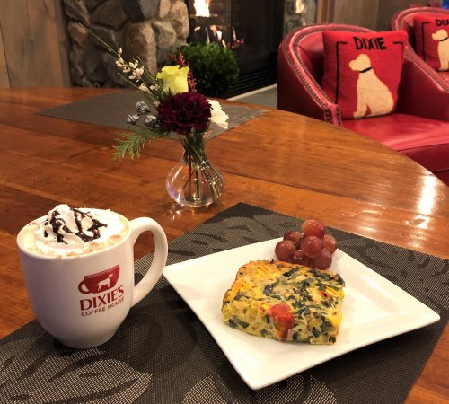 A cozy table setting with a mug of hot chocolate, a plate of vegetable frittata, grapes, and a vase of flowers.