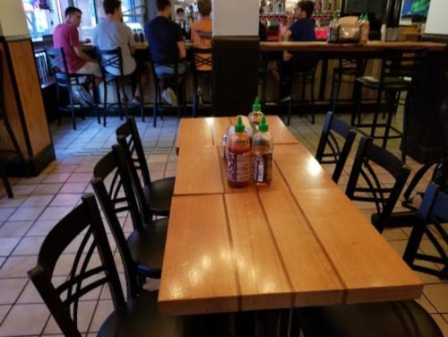 A wooden table with condiments sits in a casual dining area, with patrons visible in the background.