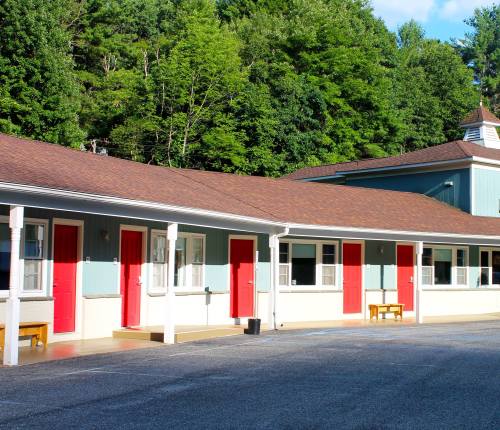 A row of motel rooms with red doors, surrounded by green trees and a blue sky.