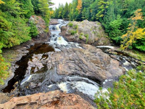 A scenic view of a waterfall cascading over rocky terrain, surrounded by lush green trees and autumn foliage.