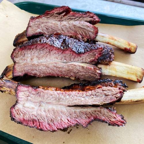 Four juicy beef ribs with a smoky crust, resting on brown butcher paper.