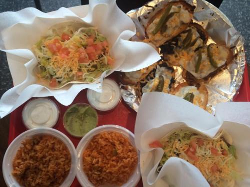 A colorful spread of tacos, rice, and sauces on a red tray, featuring fresh toppings and melted cheese.