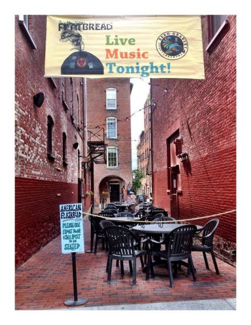 A narrow alley with outdoor seating, a banner for live music, and a sign for American flatbreads.