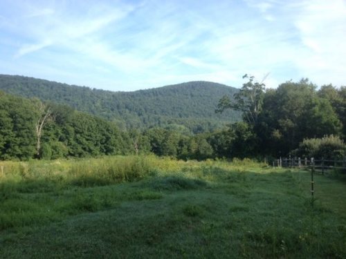 A serene landscape featuring rolling green hills under a clear blue sky, with trees lining the foreground.