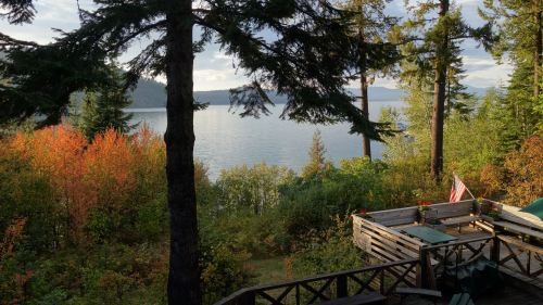 Scenic view of a lake surrounded by trees and colorful foliage, with a wooden deck and an American flag in the foreground.
