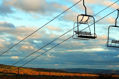 A scenic view of a landscape with autumn foliage, featuring empty ski lift chairs against a cloudy sky.