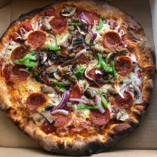 A pizza topped with pepperoni, mushrooms, green peppers, and red onions in a cardboard box.