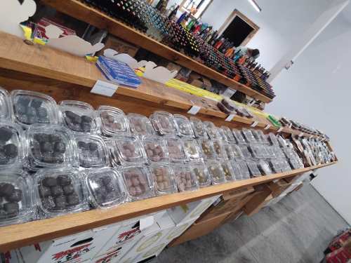 A display of assorted chocolates in clear containers on a wooden shelf, with various products in the background.