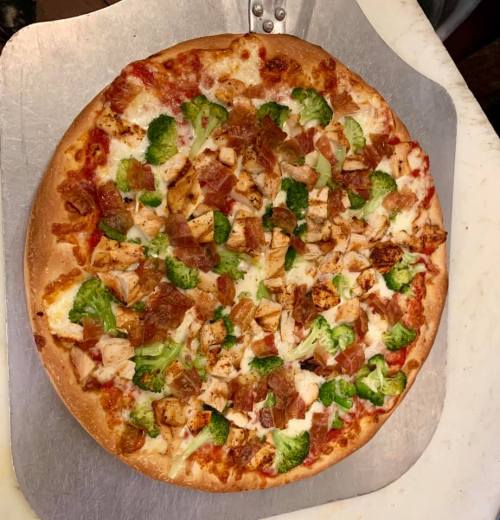 A freshly baked pizza topped with chicken, bacon, broccoli, and cheese on a golden crust.