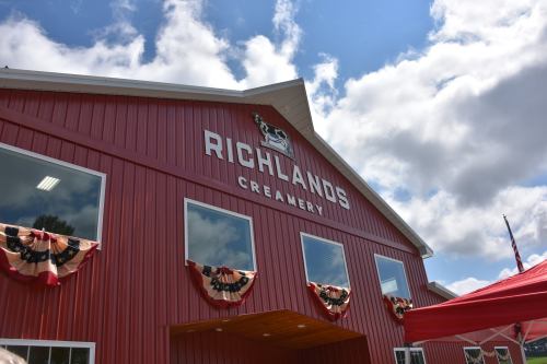 Red barn-style building with "Richlands Creamery" sign, decorated with bunting under a blue sky with clouds.