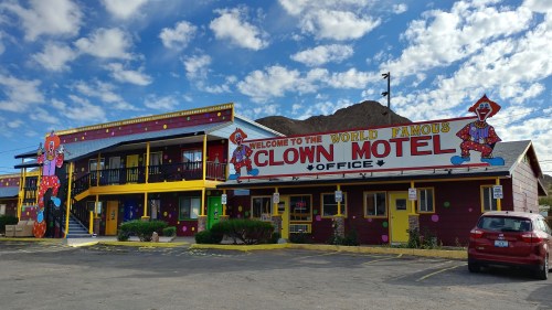 Colorful exterior of the Clown Motel, featuring clown murals and a sign welcoming visitors, under a blue sky with clouds.