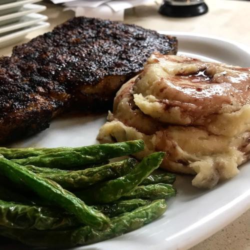 A plate featuring a grilled steak, creamy mashed potatoes with gravy, and sautéed green beans.