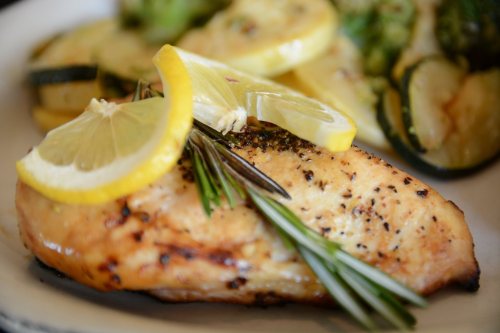 Grilled chicken breast garnished with lemon slices and rosemary, served with sautéed zucchini and yellow squash.